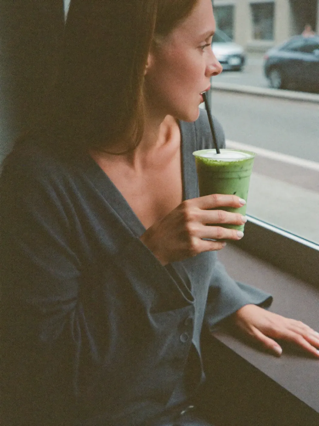 A woman drinking an iced matcha by a window