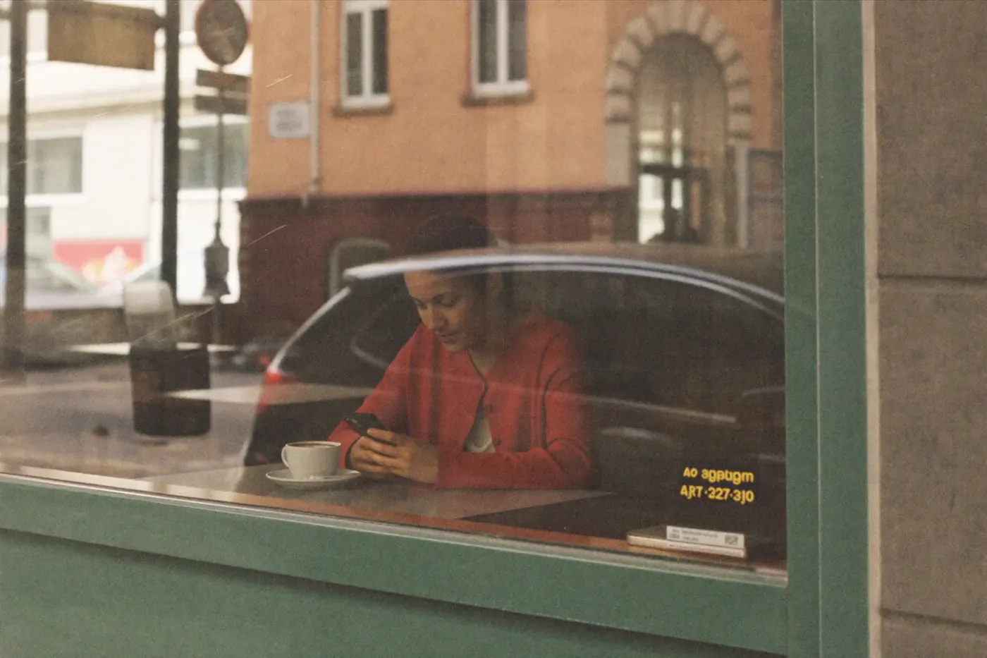 A woman in a red cardigan on her phone in a cafe window
