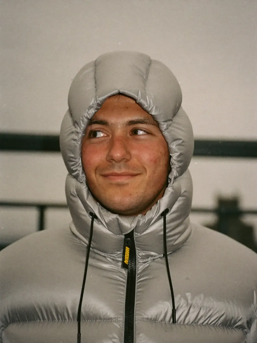 A man in a puffer jacket looking up with a small smile